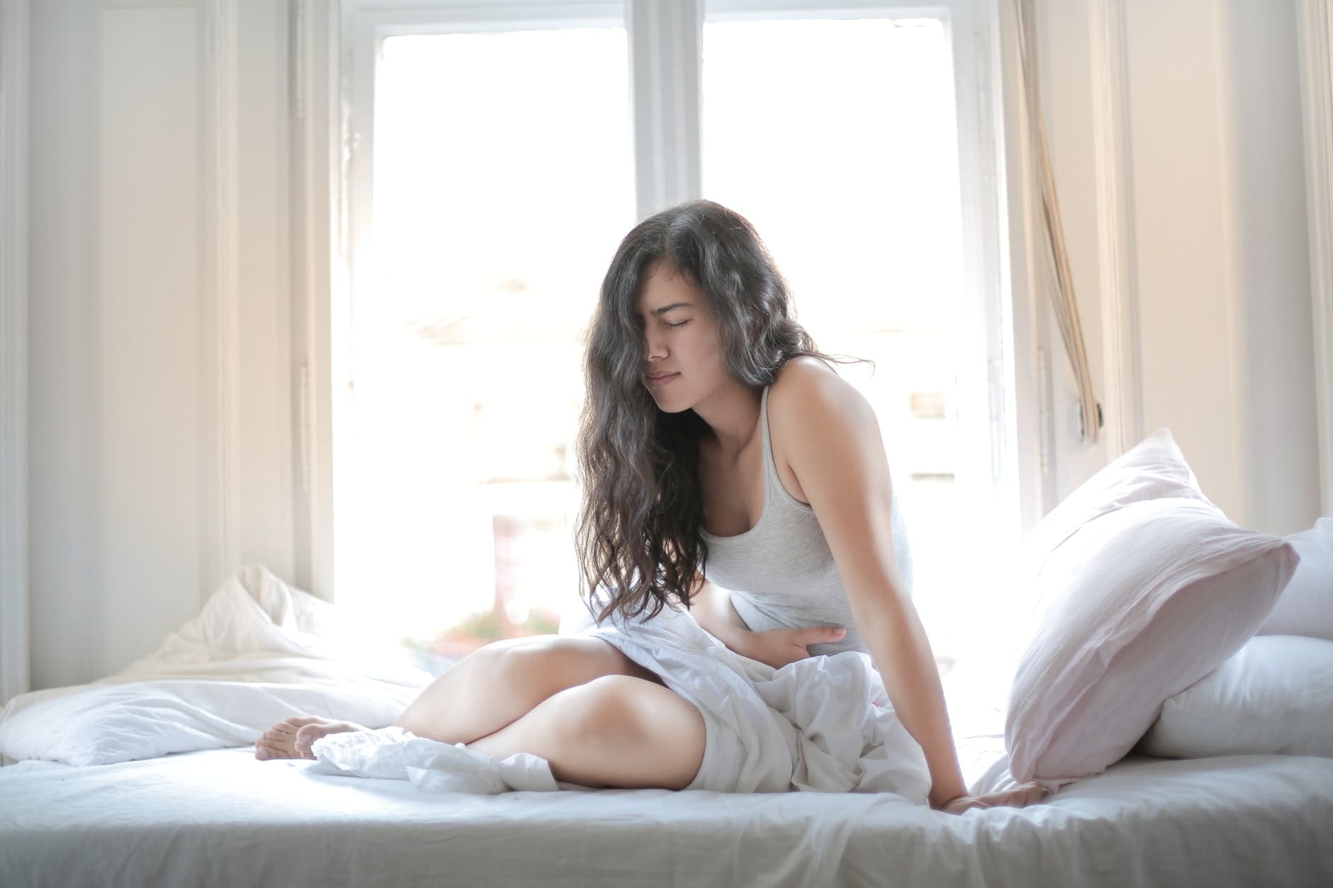woman sitting on bed experiencing IBS symptoms